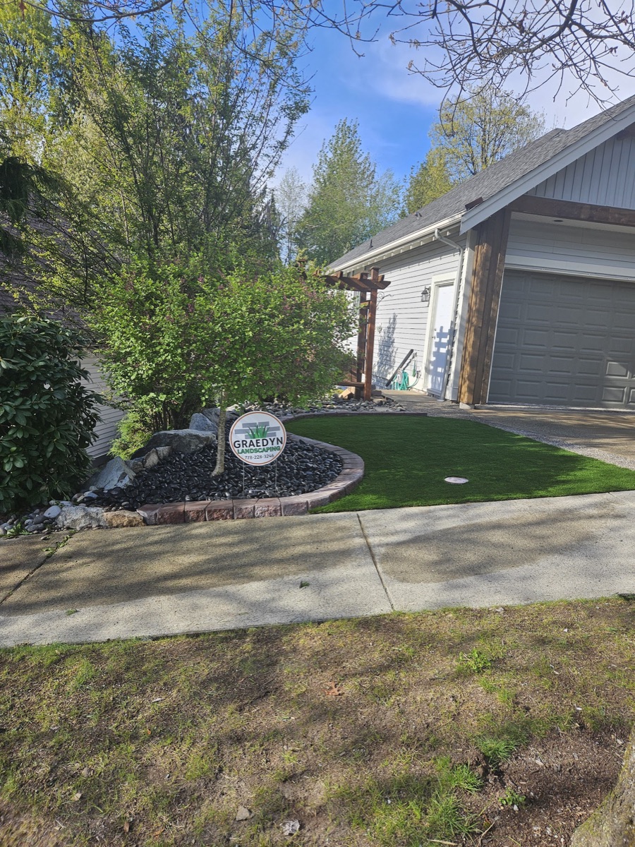 Front-yard artificial turf lawn with a stacked-paver garden border in Langley