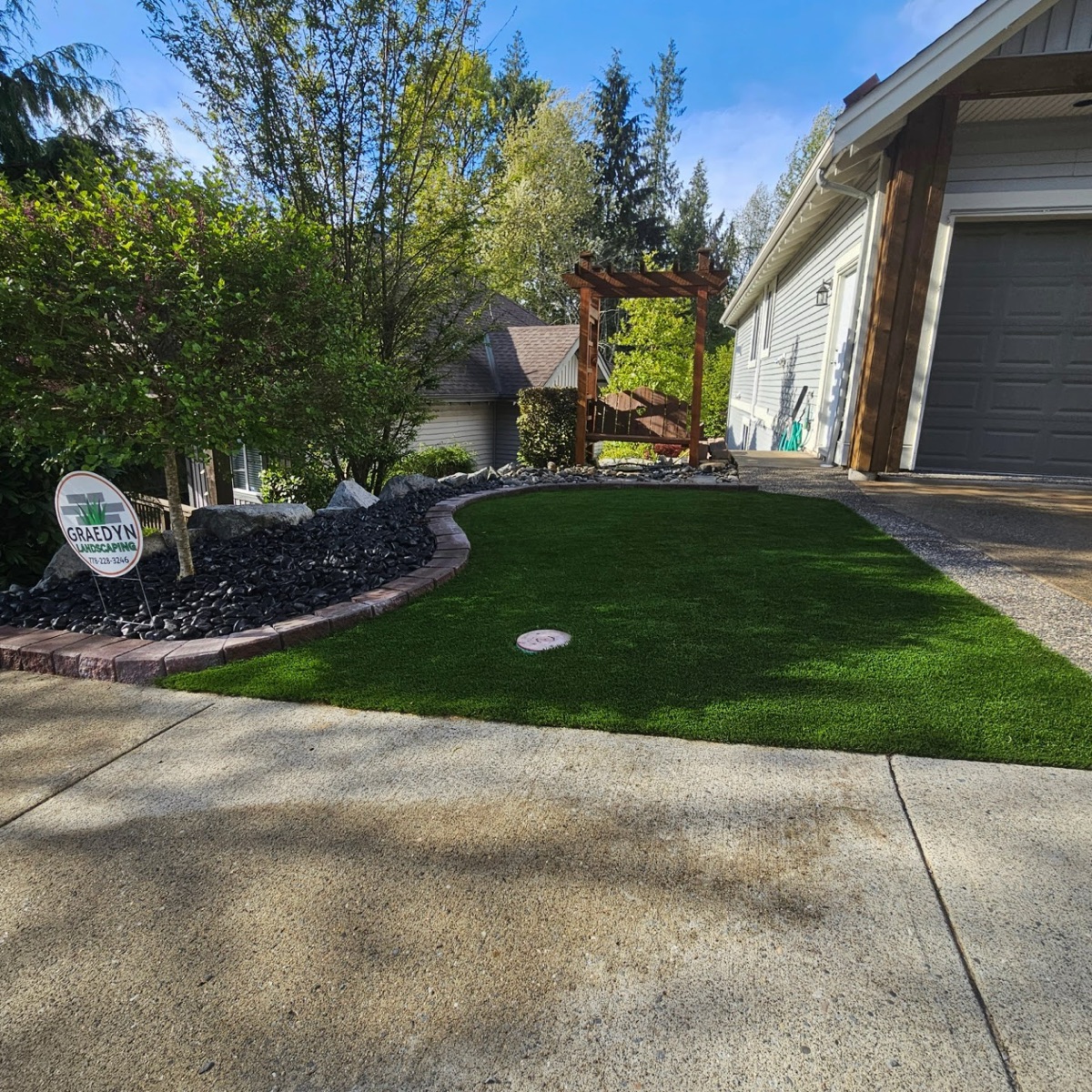 Front-yard artificial putting green with a curved paver border and river-rock bed at a Langley home