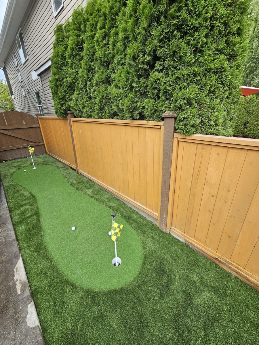 Side-yard artificial turf putting green with flags along a cedar fence in Langley