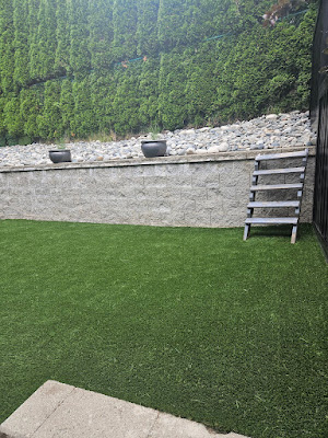 Stacked natural-stone retaining wall above an artificial turf lawn in Langley